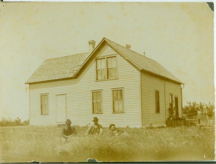 Three men sitting in the grass in front of a house