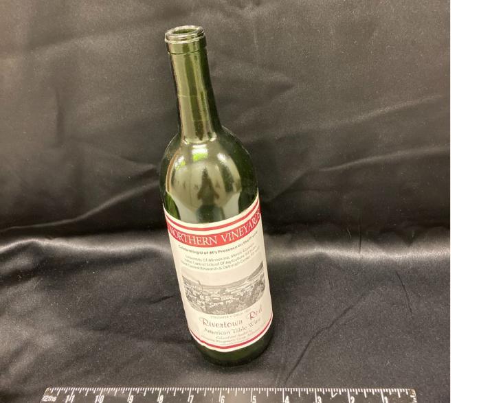 wine bottle with UMM label celebrating the anniversary of 90 years of the West Central School of Agriculture and 40 years of the University of Minnesota Morris, fall 2000. Wine name, Rivertown Red, American Table Wine, green bottle  with white and maroon label.