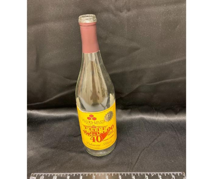 wine bottle with UMM label celebrating the anniversary of 90 years of the West Central School of Agriculture and 40 years of the University of Minnesota Morris, fall 2000. Wine name, Delaware Blush, clear bottle with maroon and gold label.
