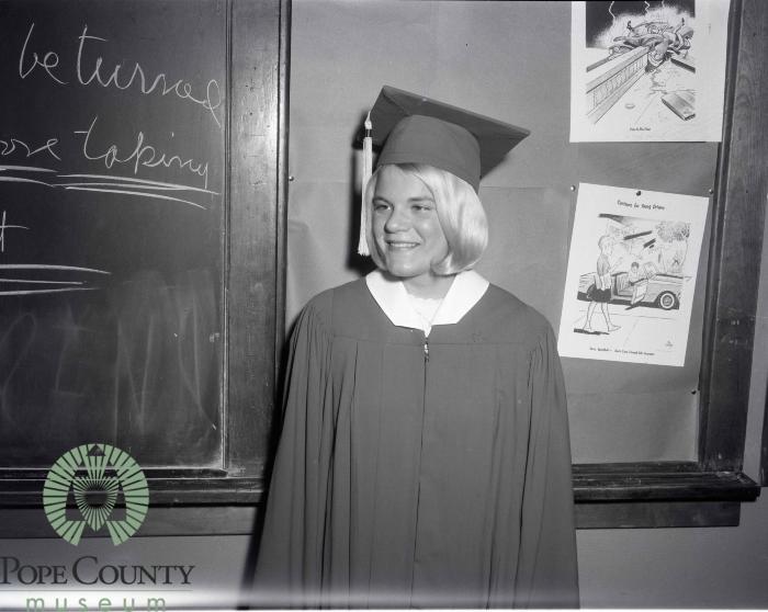 Kristin Kinney standing in a classroom dressed in her cap and gown