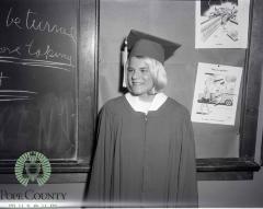 Kristin Kinney standing in a classroom dressed in her cap and gown