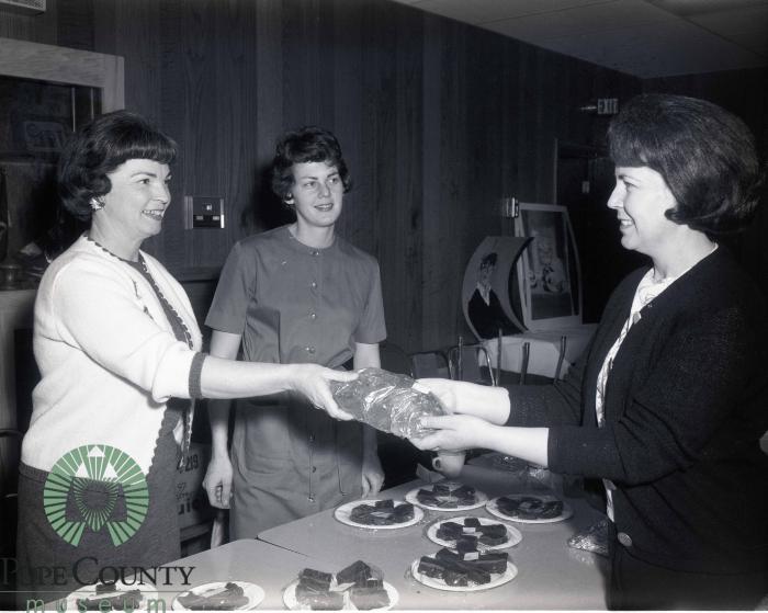 Mrs. Gerald Demars and Martha Rolig handing bread to Maurine Fjoslien