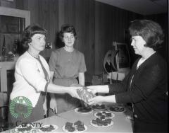 Mrs. Gerald Demars and Martha Rolig handing bread to Maurine Fjoslien