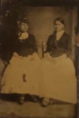 Tintype studio photograph of two women in white skirts and black shirts