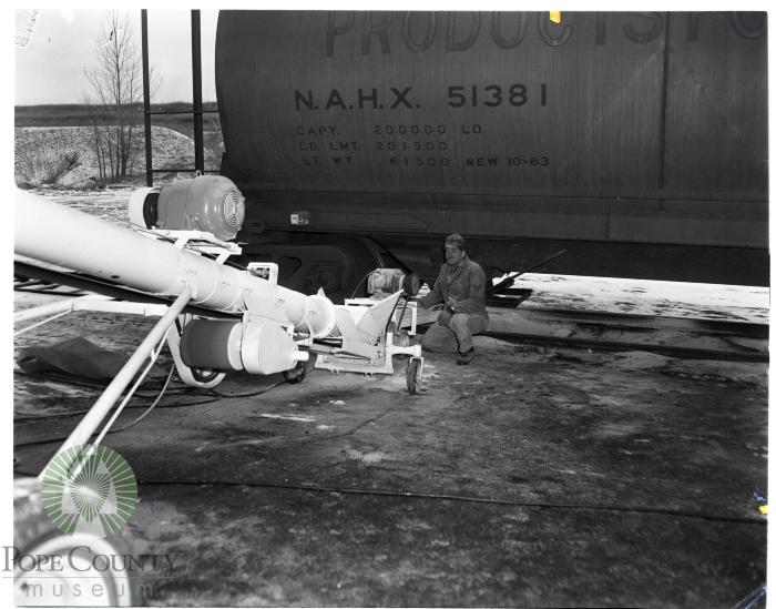 Workman watches elevator take potash from railroad car to warehouse