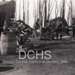 Black and white photograph of men working a saw with chunks of lumber around them