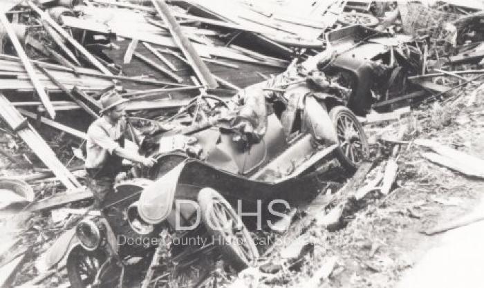 Black and white photograph of man looking at cars damaged by tornado