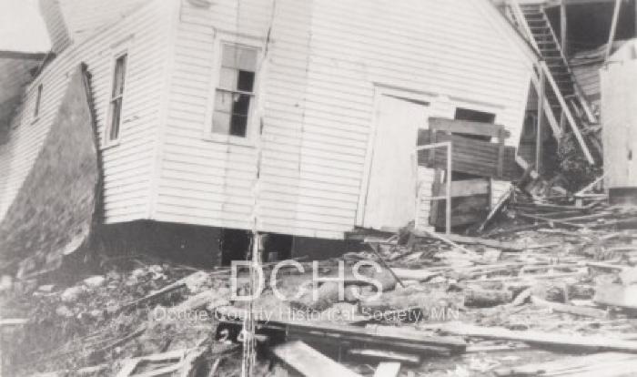 Black and white photograph of tilted house and debris from tornado