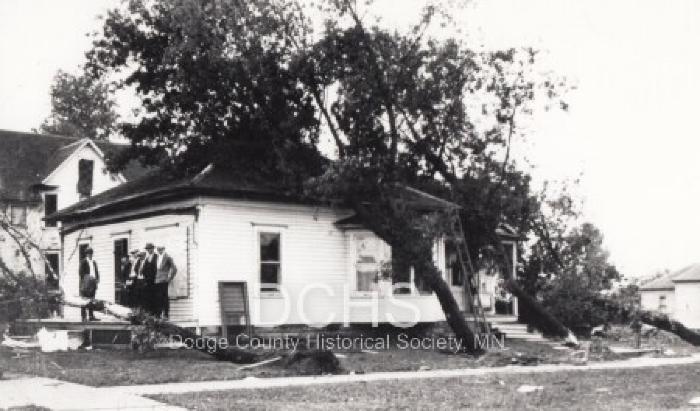Black and white photograph of house with trees felled on it
