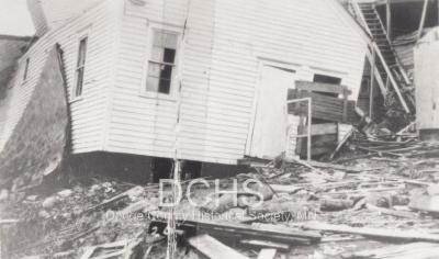 Black and white photograph of tilted house and debris from tornado